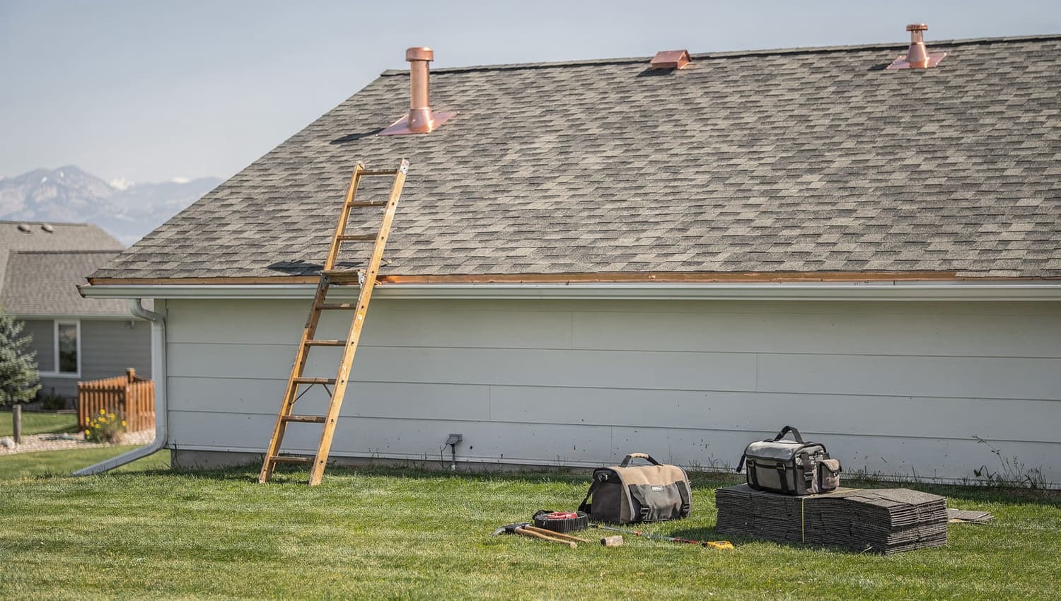 A ladder against the eave of a Centennial home with roofing tools ready on the grass